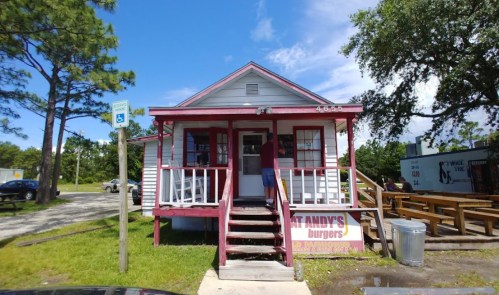A small, white house with a red trim, featuring a sign for "Andy’s Burgers" and outdoor seating nearby.