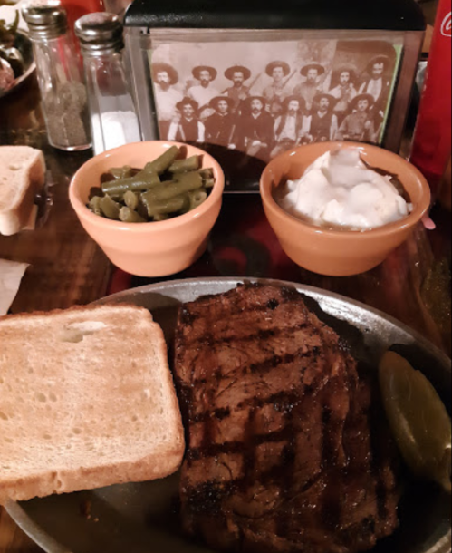 A plate with grilled steak, toast, green beans, and a bowl of sour cream, with a vintage photo of people in the background.