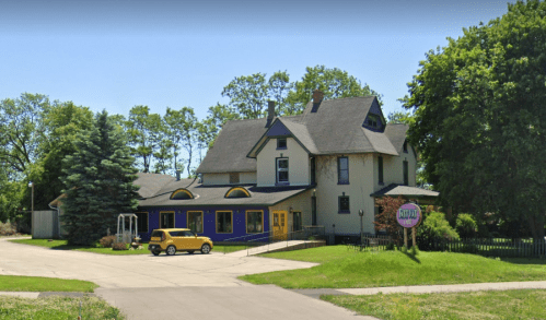 A large, colorful house with a yellow car parked outside, surrounded by trees and a grassy area.