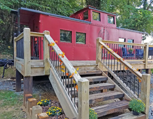 A red caboose on a wooden platform with stairs, surrounded by flowers and greenery.