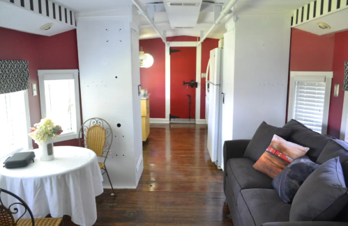 Cozy interior of a small home with a sofa, dining table, and kitchen area, featuring red walls and wooden floors.