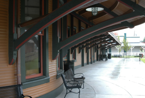 A covered walkway with benches, featuring wooden arches and a smooth concrete floor, in a quiet outdoor setting.