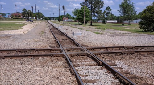 A view of intersecting railway tracks surrounded by gravel and grass under a clear blue sky.