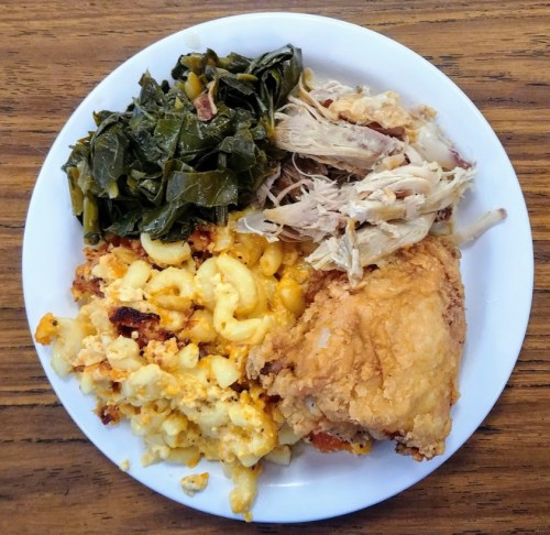 A plate of food featuring fried chicken, collard greens, shredded chicken, and macaroni and cheese.