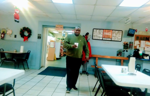 A man in a green sweater walks through a casual dining space with tables and a festive decor.