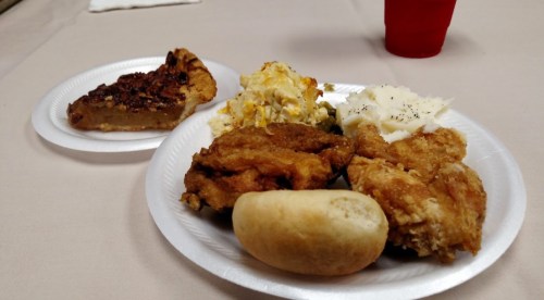 A plate of fried chicken, mashed potatoes, macaroni and cheese, a roll, and a slice of pecan pie on a table.
