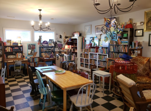 Cozy room filled with bookshelves, a large table, colorful chairs, and eclectic decor, creating a warm reading space.
