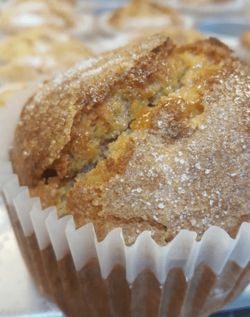 Close-up of a freshly baked muffin with a golden-brown top, sprinkled with sugar, in a white paper liner.