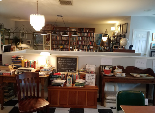 Cozy reading nook with bookshelves, a chalkboard, and tables filled with books and decor in a warm, inviting space.