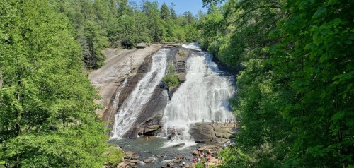 A scenic waterfall surrounded by lush greenery, with people enjoying the area at its base.
