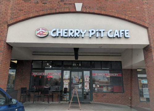 Exterior of Cherry Pit Cafe, featuring a sign and large windows, with an open sign and a menu displayed outside.