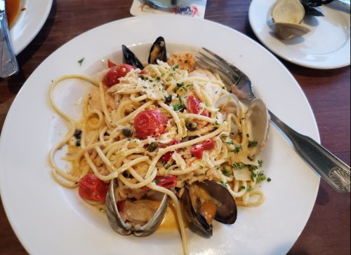 A plate of linguine with clams, mussels, cherry tomatoes, and herbs, garnished with parsley.