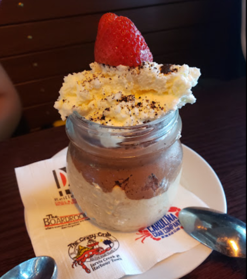 A dessert in a jar featuring layers of chocolate mousse, whipped cream, and a strawberry on top, served on a napkin.