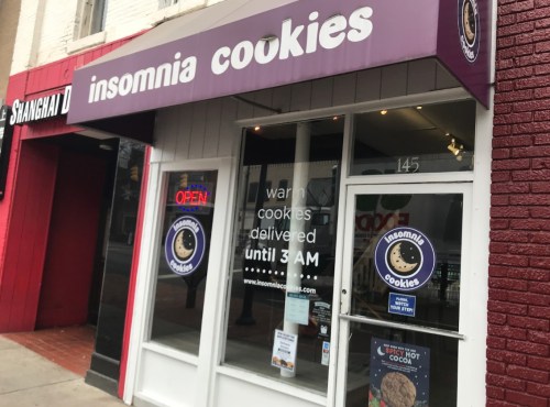 Exterior of Insomnia Cookies shop with an open sign, featuring a menu and delivery hours until 3 AM.