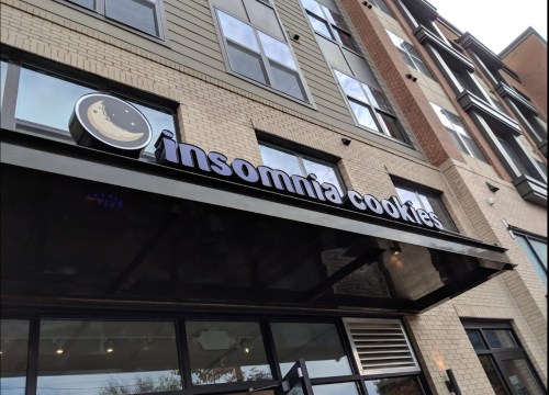Sign for Insomnia Cookies on a building exterior, featuring a moon logo and modern architecture.