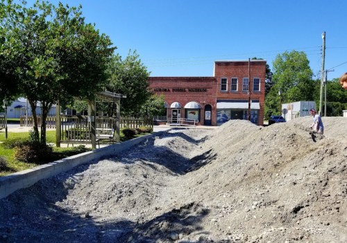 A gravel path leads to a historic brick building, surrounded by trees and a clear blue sky.