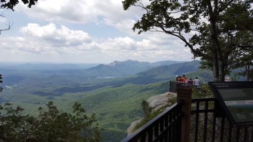 A scenic mountain view from a lookout point, with lush greenery and distant peaks under a partly cloudy sky.