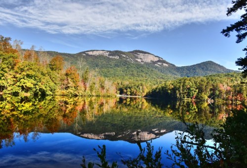 A serene lake reflects colorful autumn trees and a mountain under a clear blue sky.