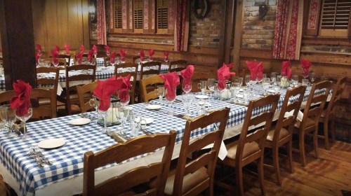 A rustic dining room with wooden tables set with blue and white checkered tablecloths and red napkins.