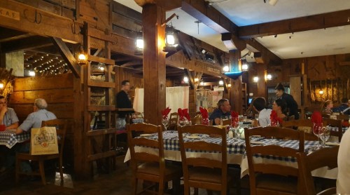 Cozy restaurant interior with wooden beams, checkered tablecloths, and diners enjoying their meals. Warm lighting ambiance.