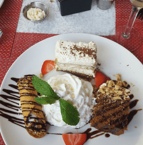 A dessert plate featuring tiramisu, a cannoli, whipped cream, and strawberries, garnished with mint leaves.