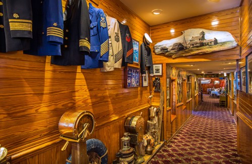 A wooden hallway lined with military uniforms and historical artifacts, leading to a warmly lit dining area.