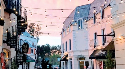 Charming street scene with string lights and pastel sky, featuring boutique shops and a spiral staircase.