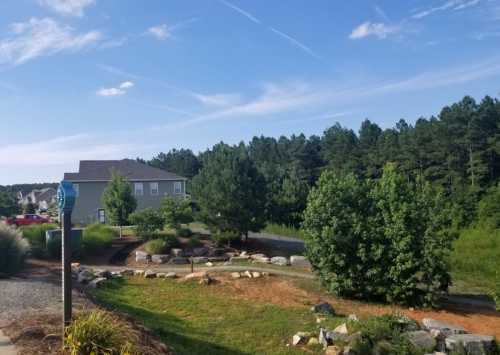 A serene landscape featuring a pathway, greenery, and a house in the background under a clear blue sky.