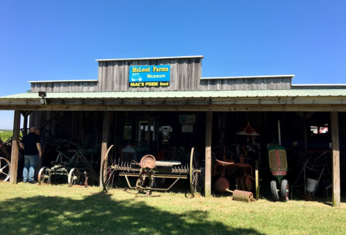 A rustic farm museum with vintage farming equipment displayed outside under a clear blue sky.