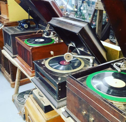 A collection of vintage gramophones with records displayed in an antique shop.