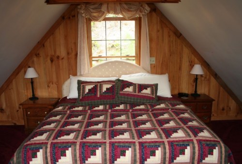 Cozy bedroom with a wooden A-frame design, featuring a quilted bedspread and two bedside lamps.