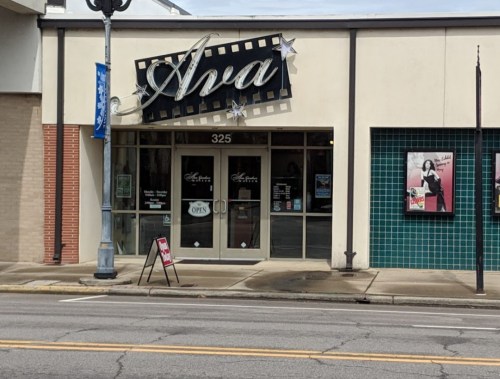Ava storefront with a marquee sign, open door, and posters on the wall, located at 325 on a city street.