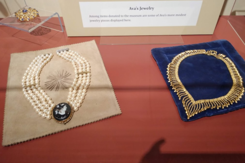 Two jewelry pieces displayed: a pearl necklace with a cameo and a gold necklace on blue fabric.