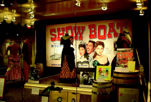 Display of costumes and memorabilia from "Show Boat," featuring vibrant dresses and promotional materials.