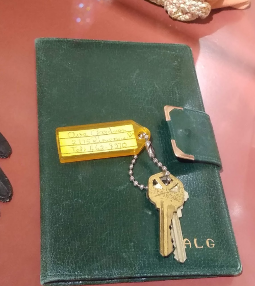 A green wallet with a keychain and a tag displaying a name, address, and phone number.