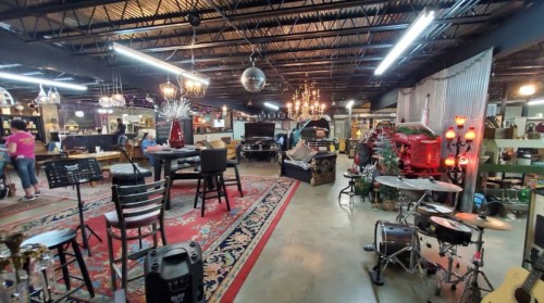 A spacious vintage shop with eclectic decor, featuring musical instruments, furniture, and decorative lights.