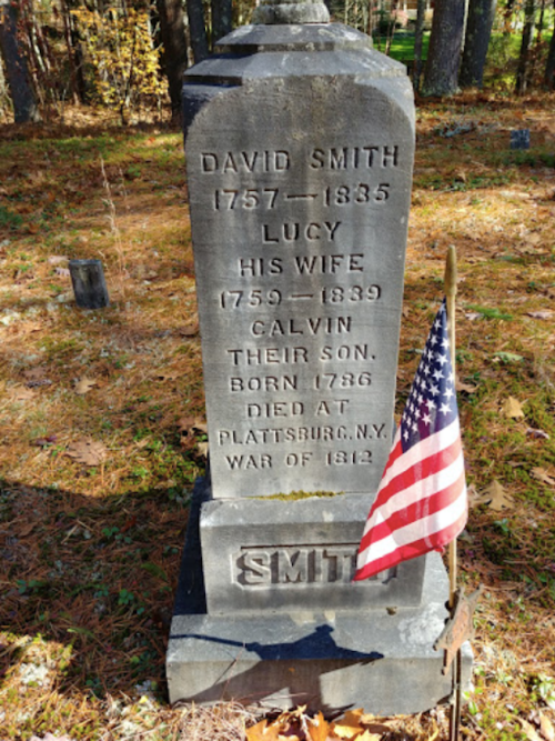 Gravestone of David Smith (1757-1835), Lucy (1759-1839), and their son Calvin, with a small American flag nearby.