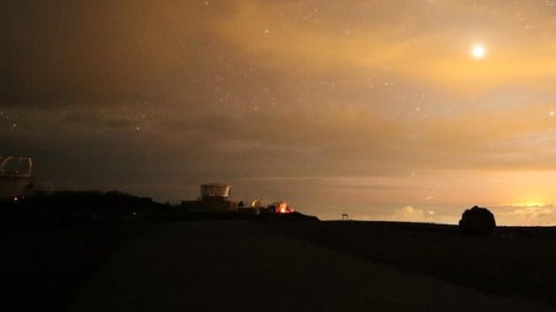 A night sky with clouds and stars, featuring a bright planet, and silhouettes of observatories on a dark landscape.