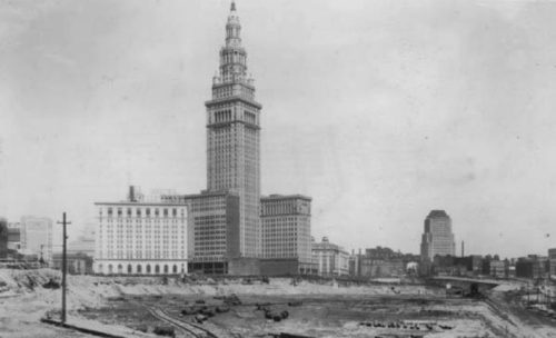 Historic black-and-white photo of a tall building under construction, surrounded by a barren landscape and machinery.