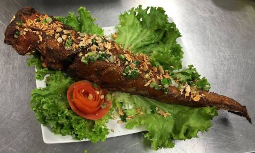 A beautifully presented whole fish garnished with herbs, nuts, and a rose-shaped tomato on a bed of lettuce.