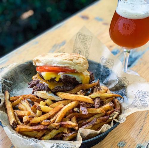 A juicy cheeseburger with tomato, served with crispy fries and a glass of beer on a wooden table.