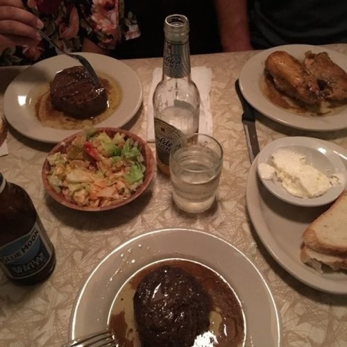 A table set with two plates of meat, a salad, drinks, and a side of bread, creating a cozy dining atmosphere.