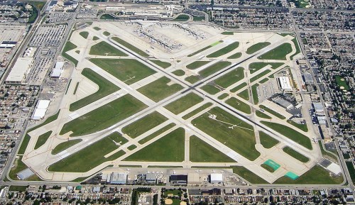 Aerial view of a large airport with multiple runways, taxiways, and surrounding green areas.