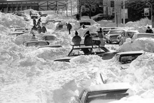A snowy street filled with abandoned cars and people navigating through deep snowdrifts.