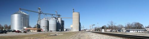 Panoramic view of grain silos and a railway track under a clear blue sky.