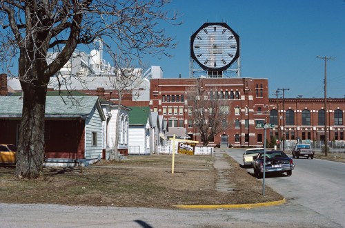 A street view featuring houses, a large clock tower, and parked cars on a clear day.
