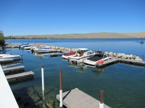 A serene marina with boats docked in clear water, surrounded by hills under a bright blue sky.