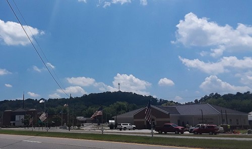 A clear blue sky with fluffy clouds over a small town, featuring a building and American flags along the roadside.