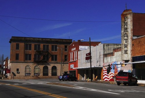 A small town street featuring a vintage theater, brick buildings, and a clear blue sky.