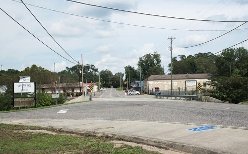 A quiet street intersection with power lines, buildings, and a police car in the distance under a cloudy sky.
